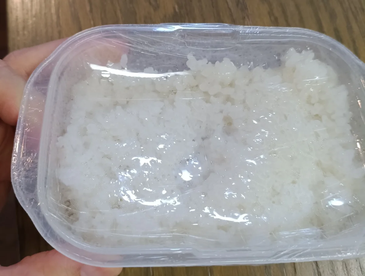 容器に白米を入れ、ラップをかけて手に持った状態