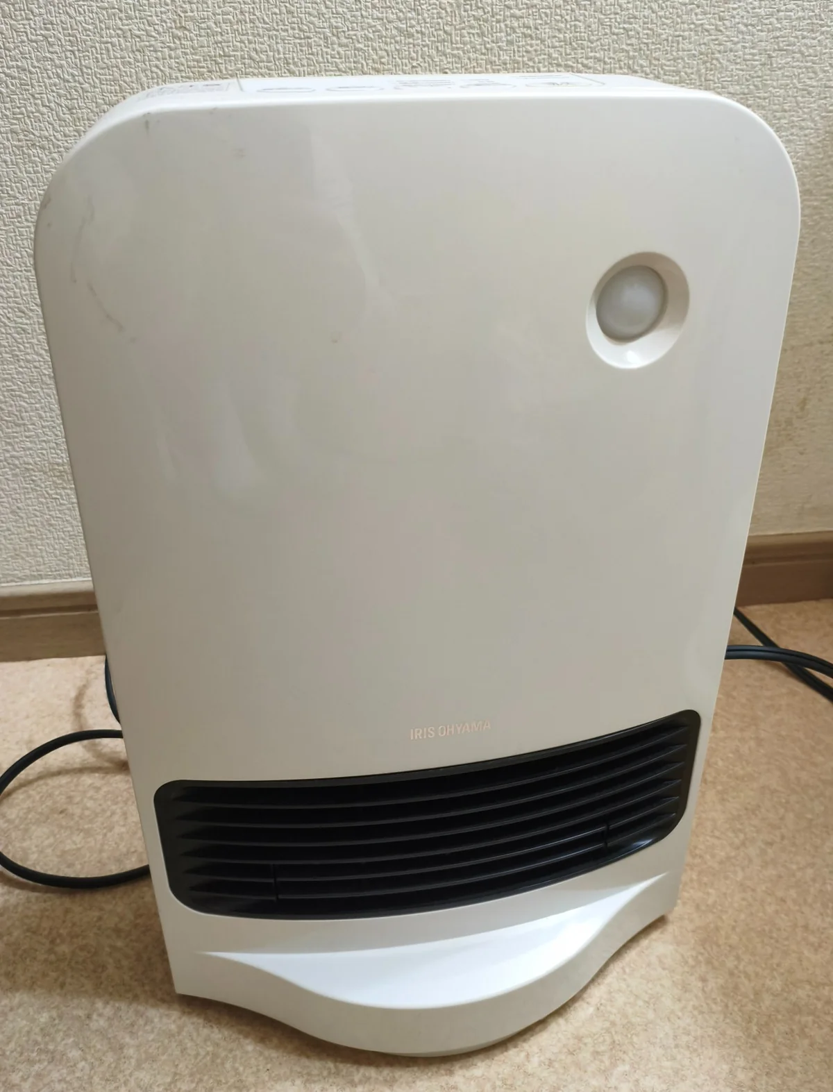 白いJCH-12TDSW1の正面。丸い人感センサーと黒い温風吹き出し口が見える。